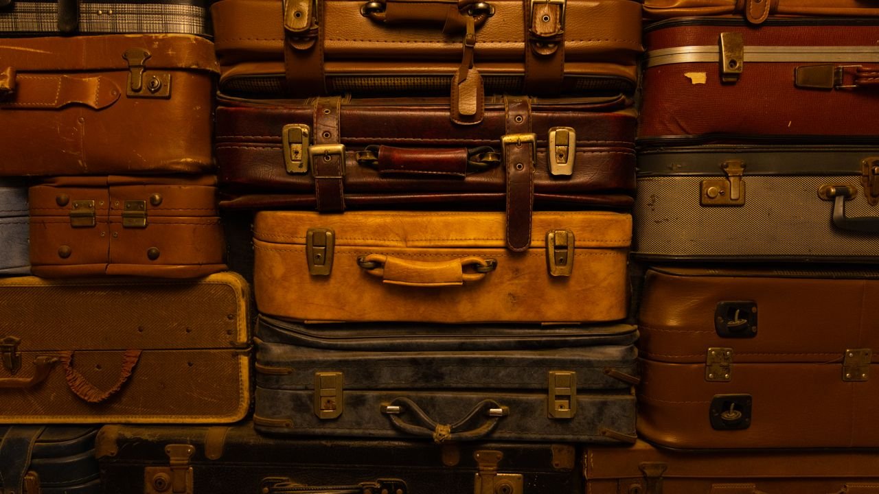 A collection of vintage suitcases stacked together, showcasing a variety of textures and colors.
