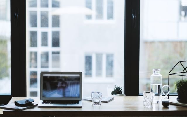 Sleek office desk setup featuring a laptop, glass of water, and open window view.