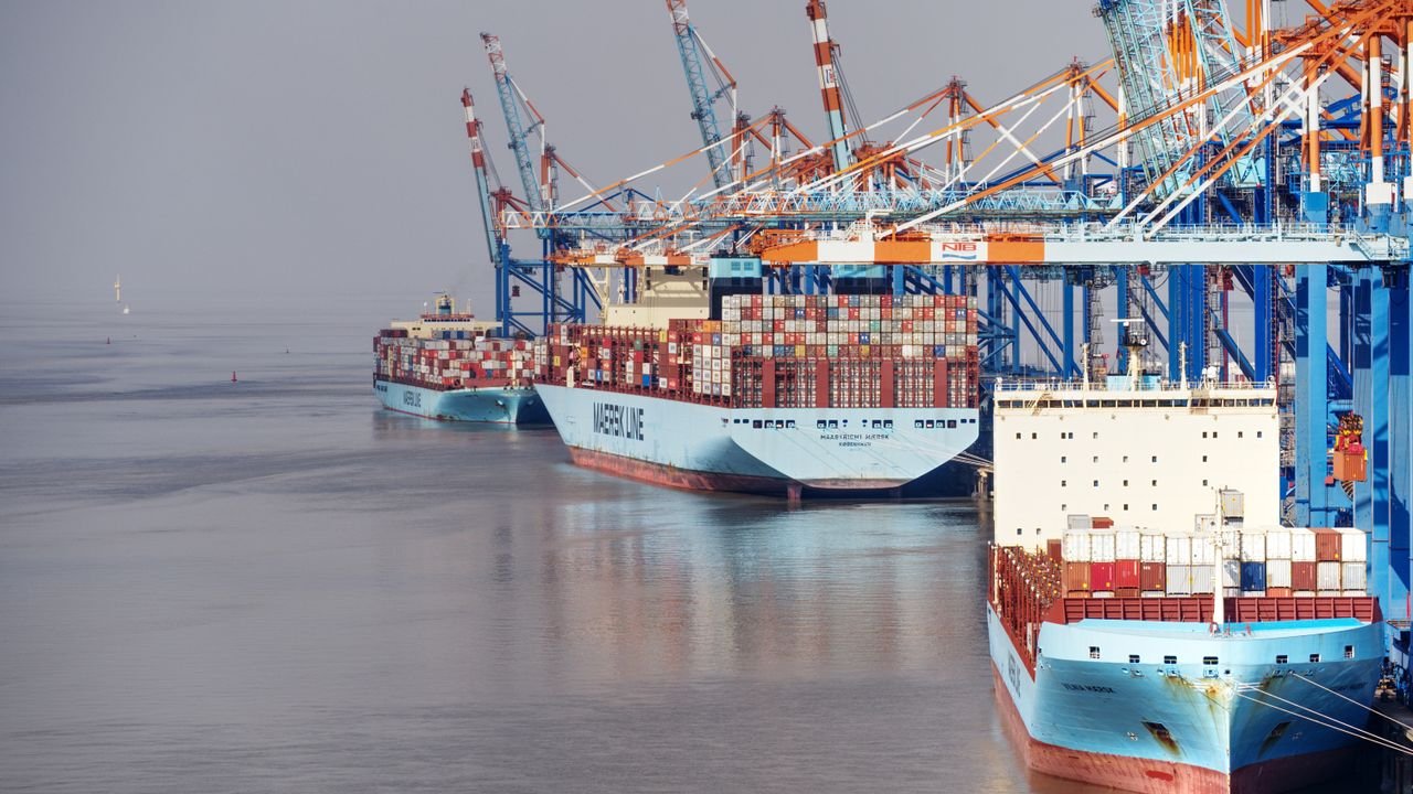 Container ships docked at a busy port with vibrant cranes and clear skies.