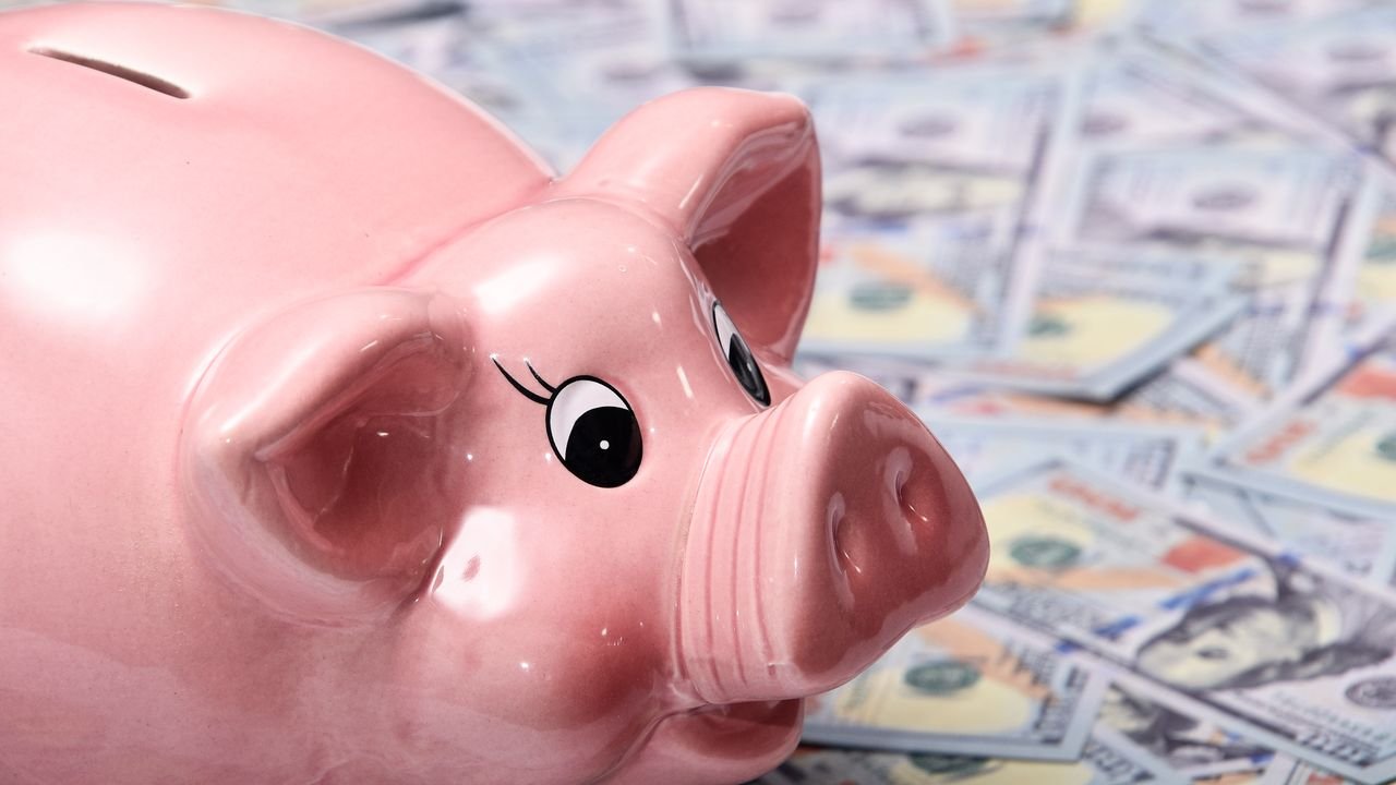 Close-up image of a shiny pink piggy bank surrounded by US hundred dollar bills, symbolizing savings and finance.