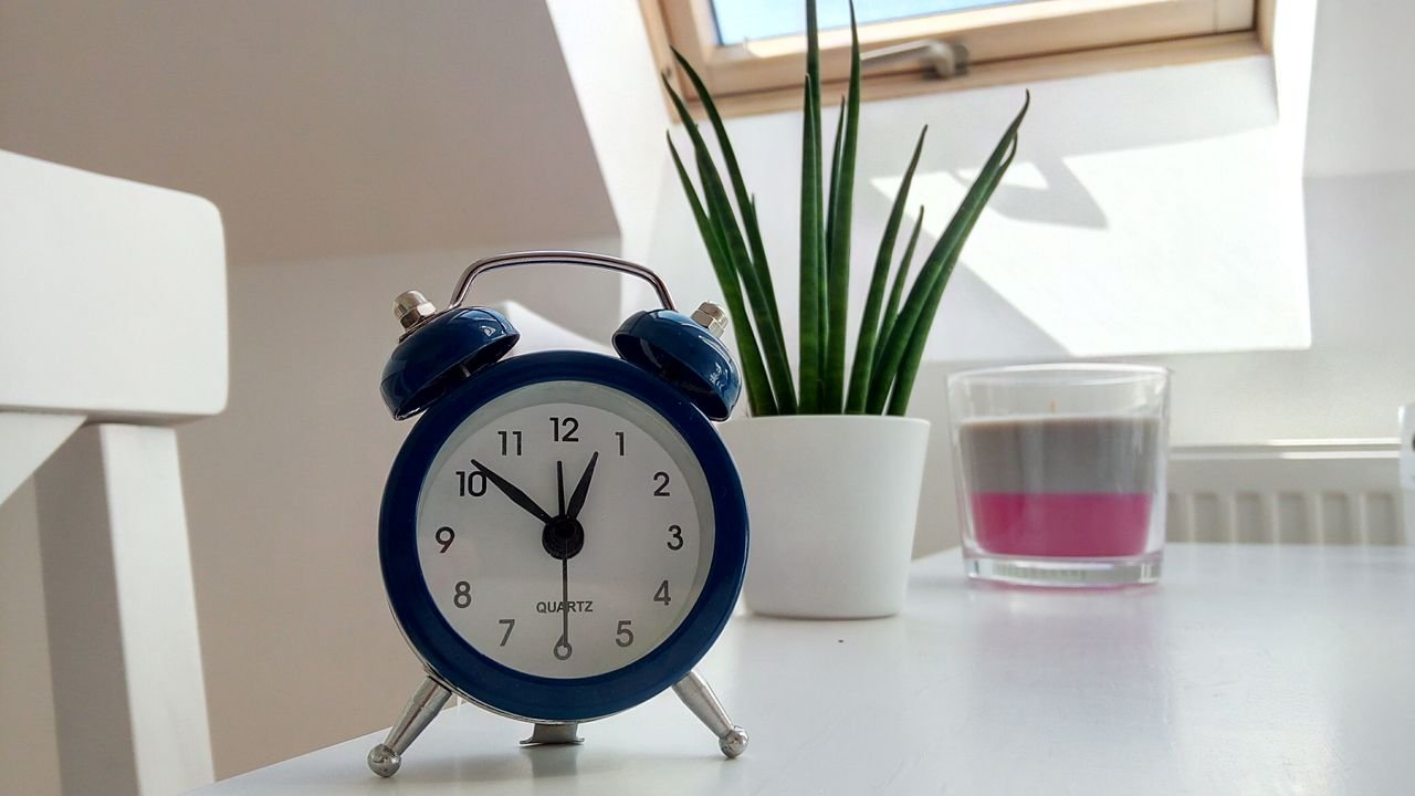 Retro blue alarm clock on a white desk with plant and candle nearby.