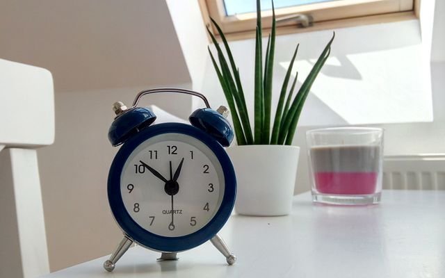 Retro blue alarm clock on a white desk with plant and candle nearby.