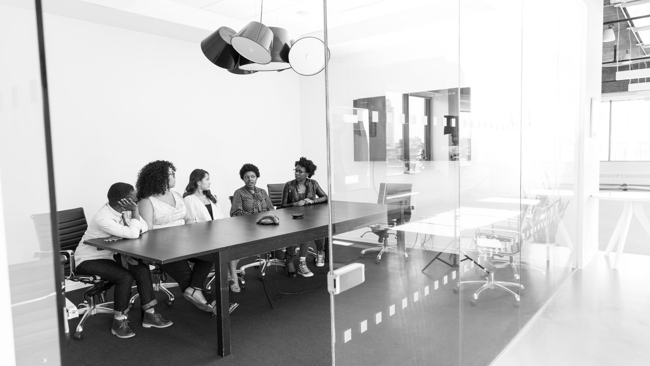 Group of professionals in a black and white office meeting discussing work around a conference table.