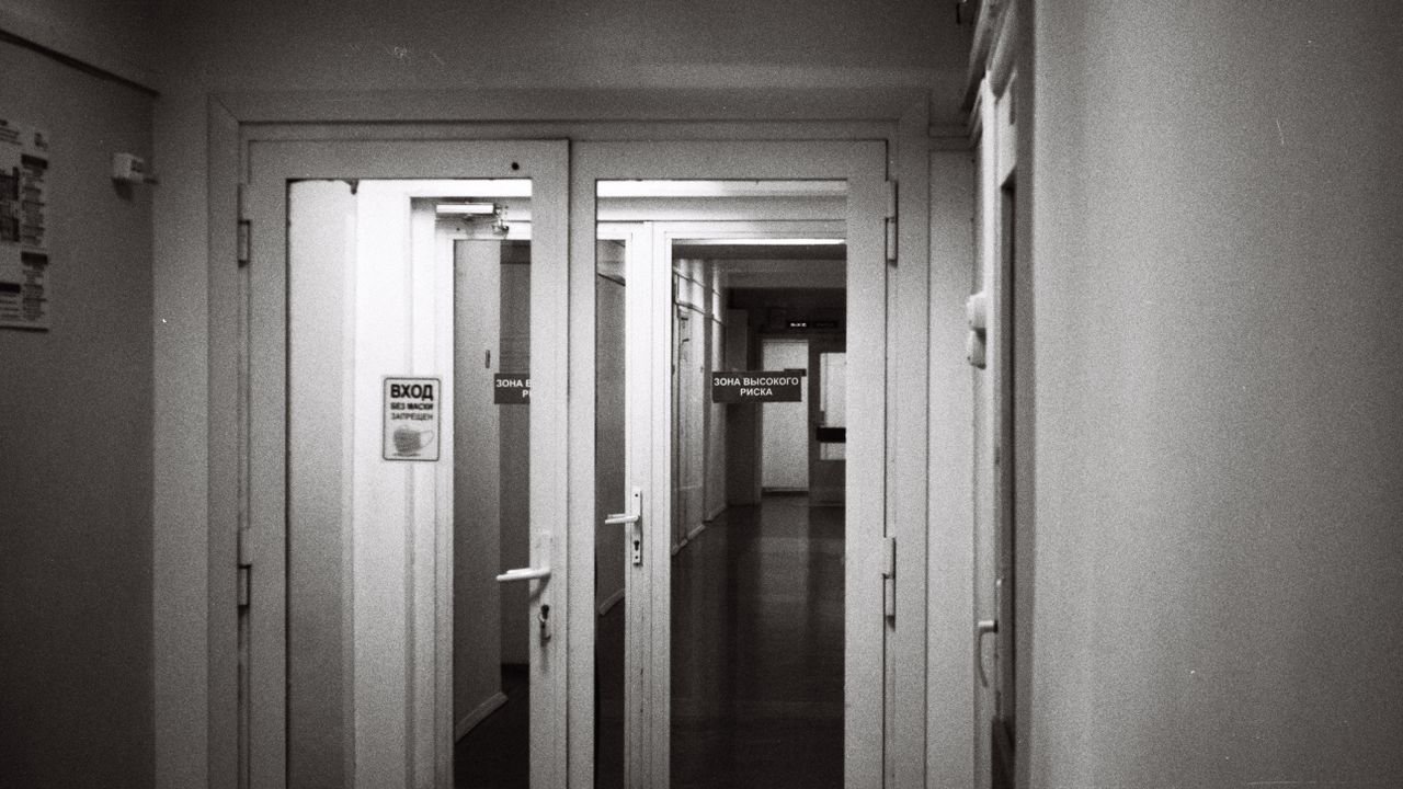 Empty hospital corridor in black and white, emphasizing open doors and healthcare environment.