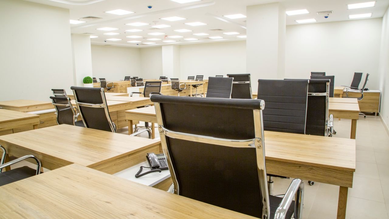 Spacious modern office with wooden desks and leather chairs in a bright, well-lit room.