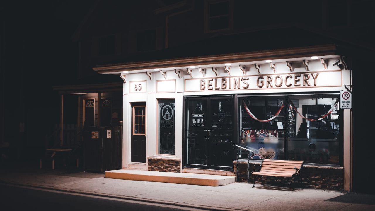Nighttime view of Belbin's Grocery storefront with warm lighting and an inviting bench.