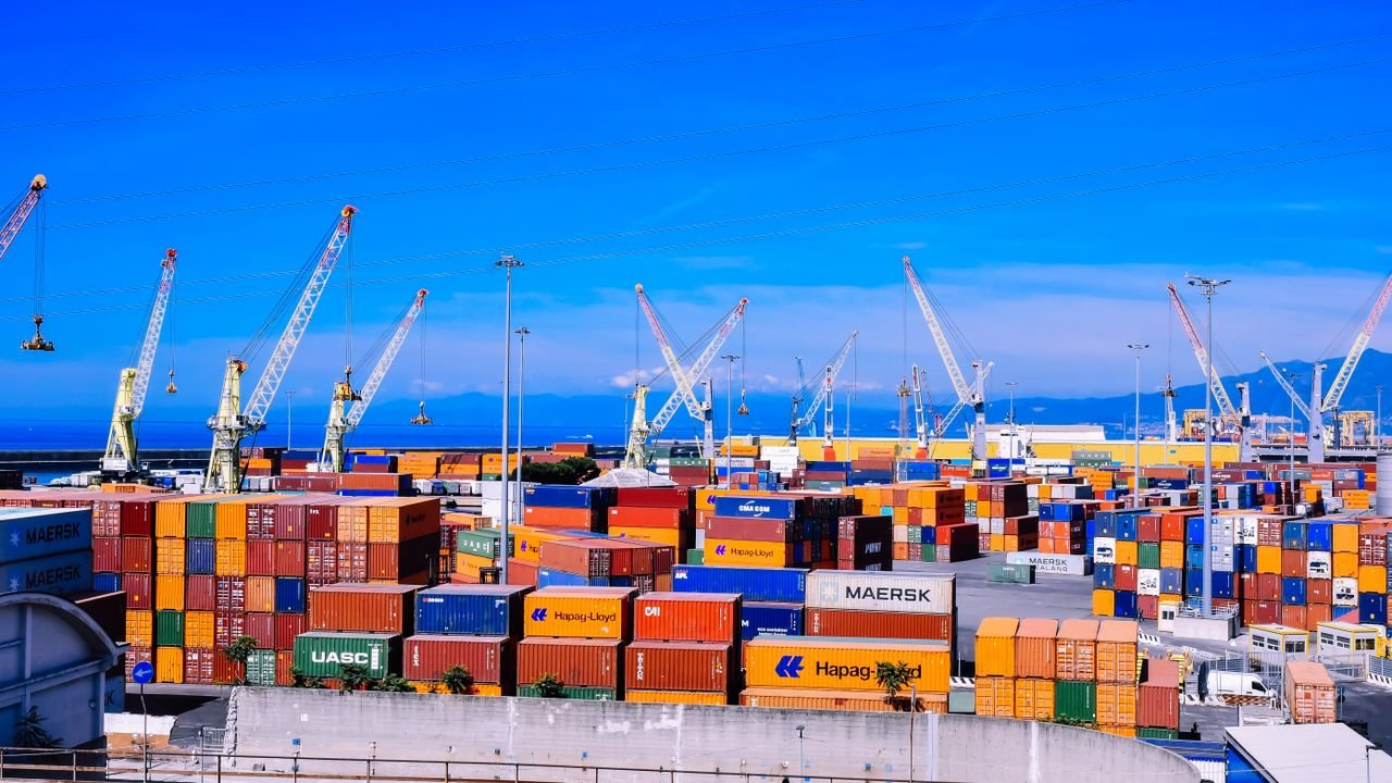 A bustling shipping port with colorful stacked containers and numerous cranes under a clear blue sky.
