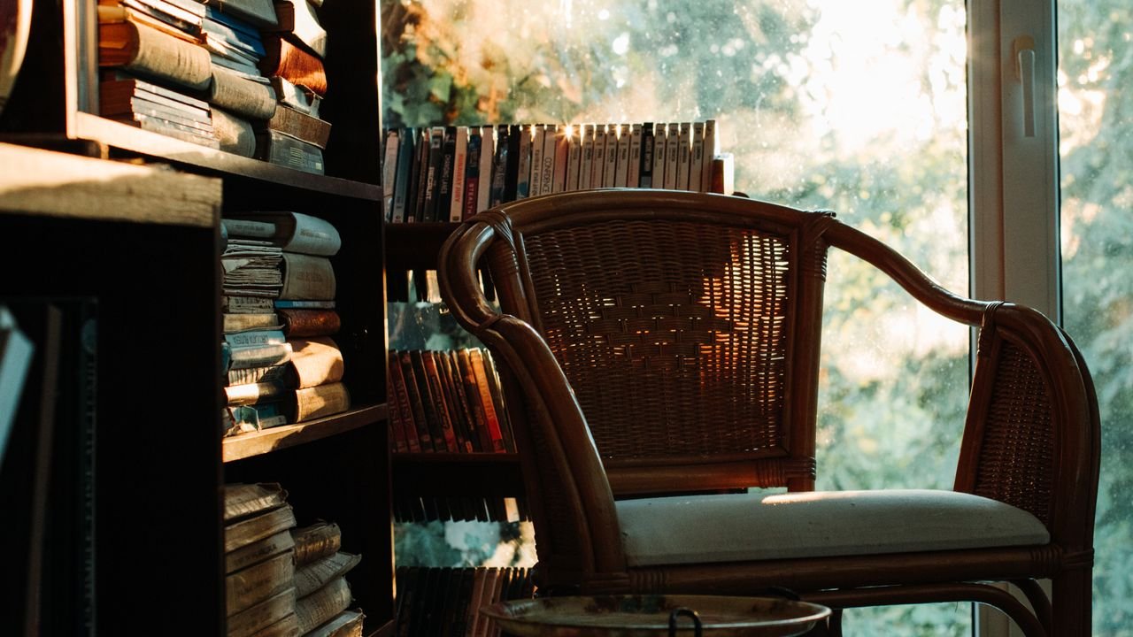 A warm, inviting reading nook with a wicker chair by a bookshelf, bathed in soft light.