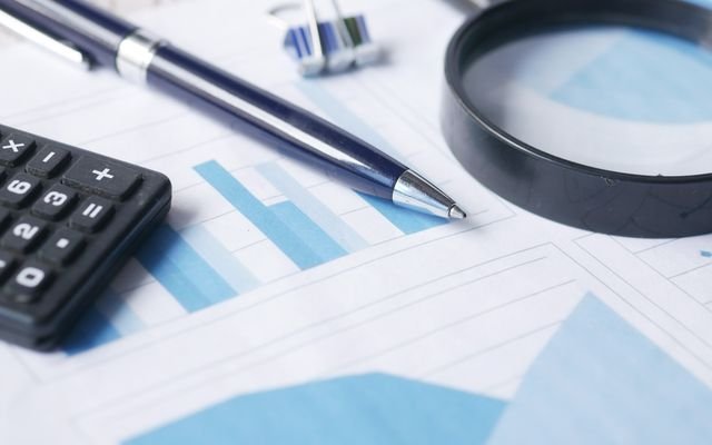 Close-up of calculator, pen, and magnifying glass on financial documents.