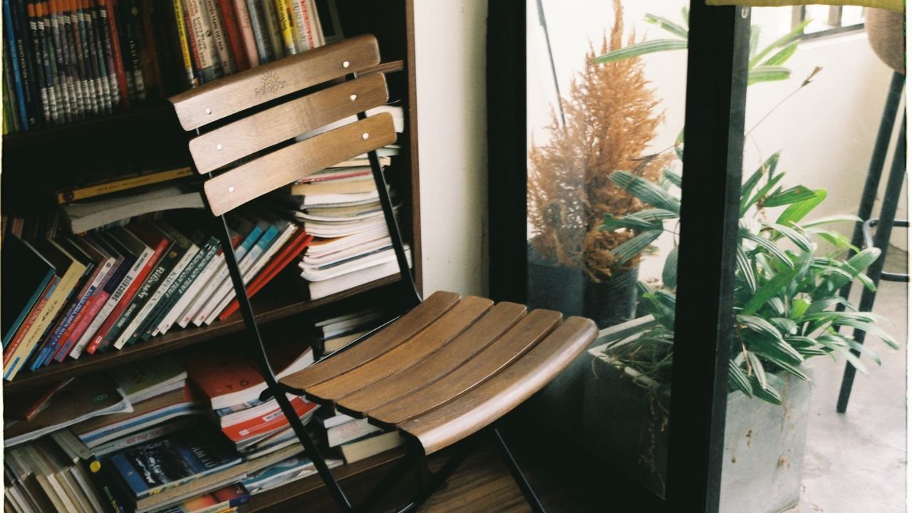 A warm, inviting space featuring a wooden chair, bookshelves, and indoor plants by a window.