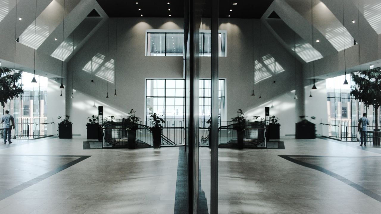 A modern, spacious indoor lobby featuring stunning architectural design and symmetrical reflections.