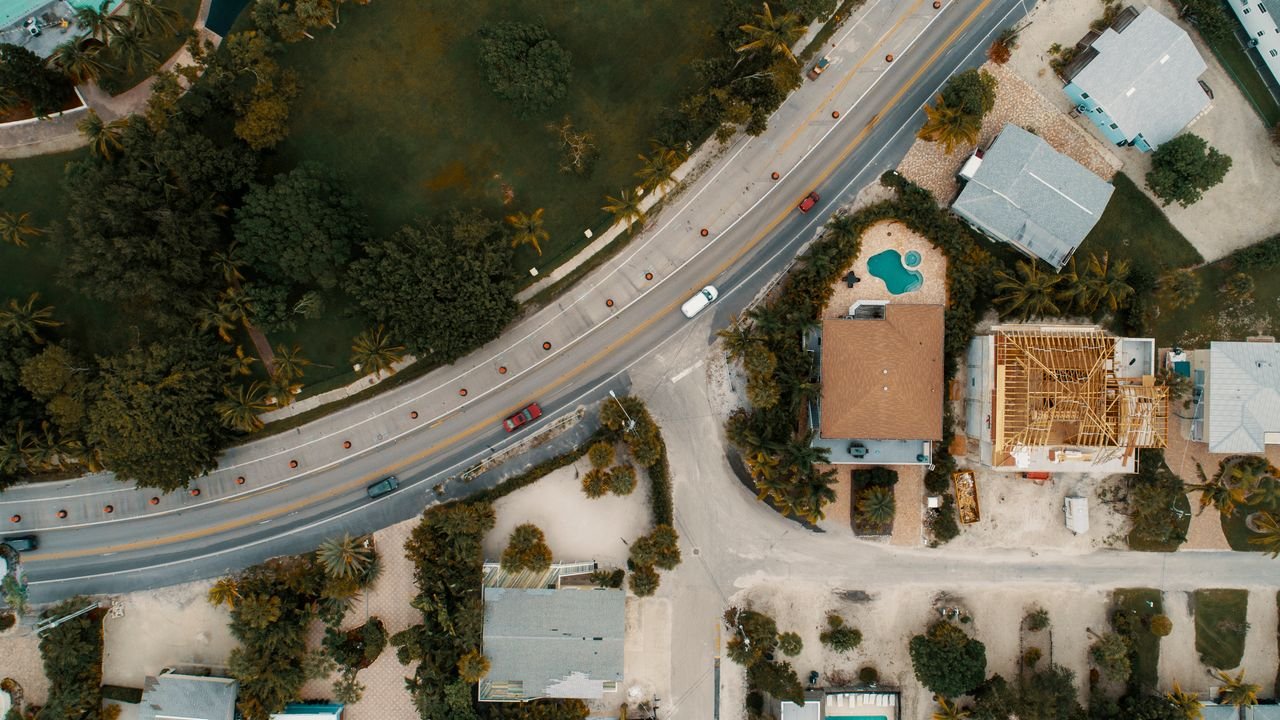 Drone view of suburban houses, road, and lush greenery, showcasing modern architecture.