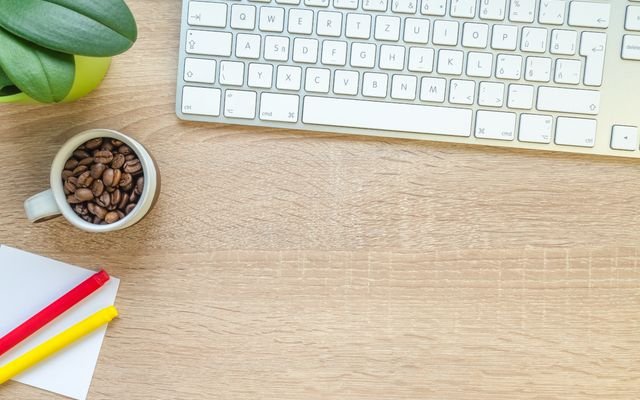 Overhead view of keyboard, coffee beans, and stationery on a wooden desk.