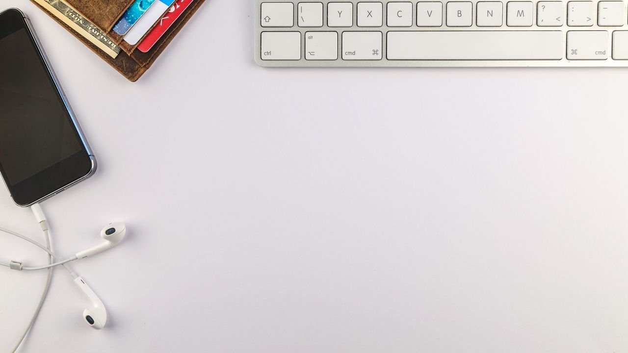 Flat lay of minimalist desk setup featuring a smartphone, keyboard, earphones, and wallet for productivity inspiration.