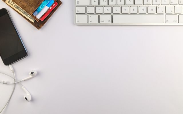 Flat lay of minimalist desk setup featuring a smartphone, keyboard, earphones, and wallet for productivity inspiration.