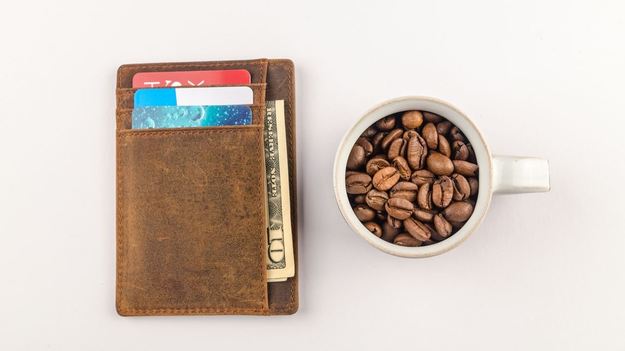 Top view of a leather wallet with credit cards and a cup filled with coffee beans on a white background.