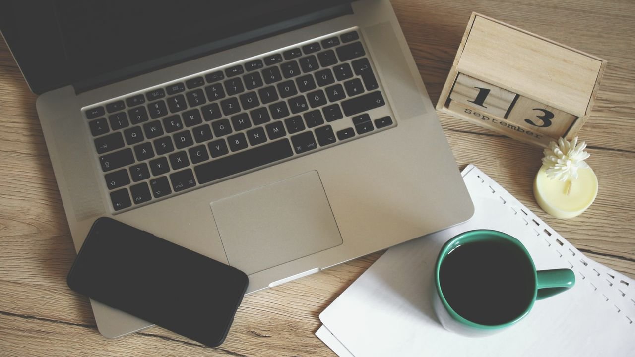 Modern office desk setup with laptop, smartphone, coffee, and calendar for productive work environment.