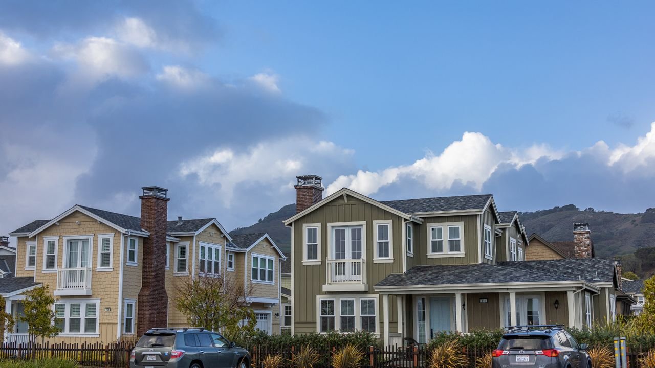 Picturesque suburban neighborhood with modern houses and parked cars under a partly cloudy sky.