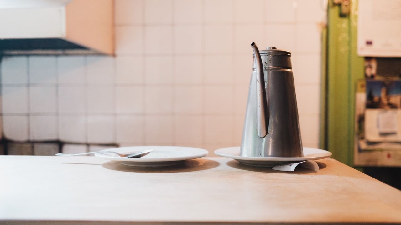 A vintage metal teapot alongside plates on a rustic diner counter.