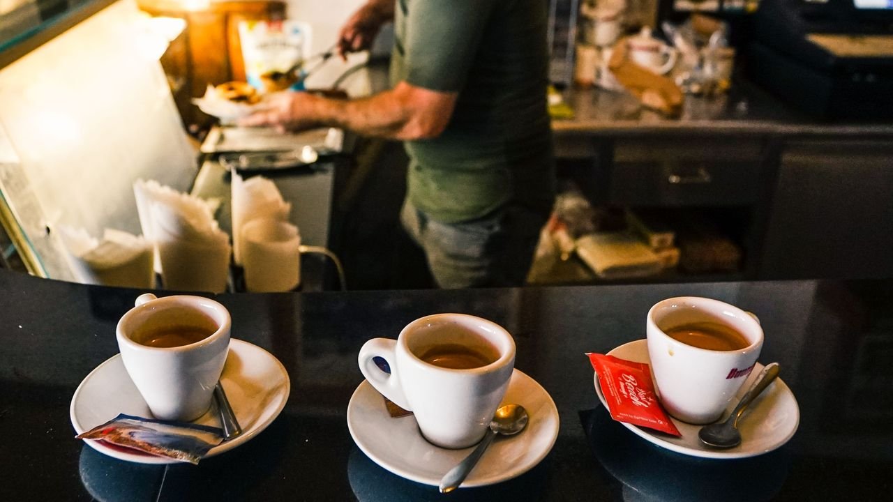 A barista in a café preparing espresso drinks on a countertop with three coffee cups in focus.