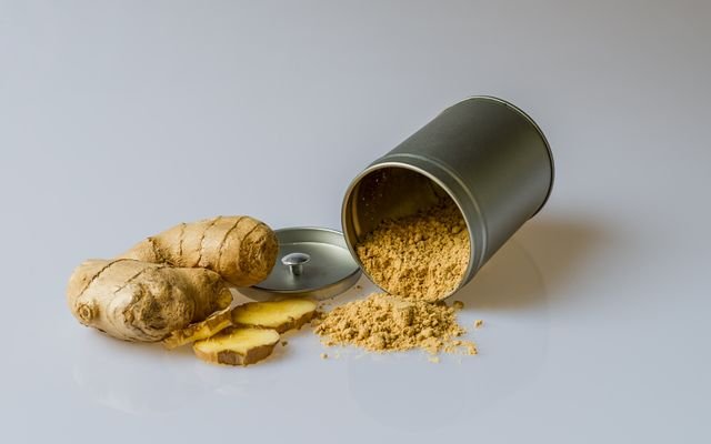 Close-up of fresh ginger root with sliced pieces and ginger powder spilled from a metal container.