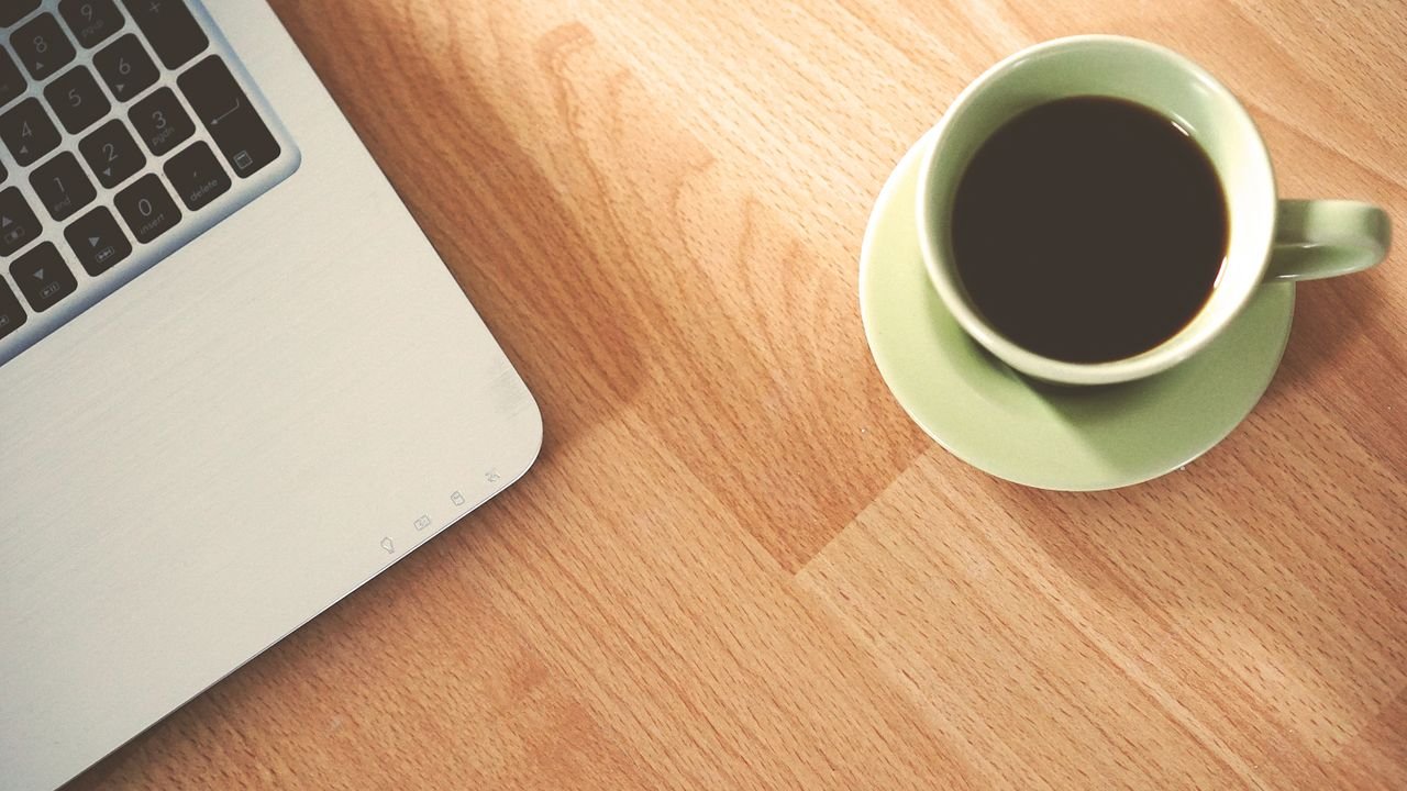 A coffee cup and laptop on a wooden desk, creating a cozy workspace vibe.