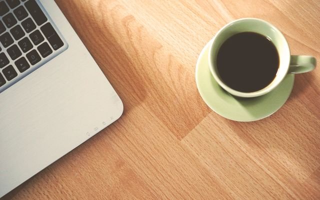A coffee cup and laptop on a wooden desk, creating a cozy workspace vibe.
