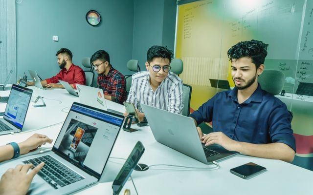 Group of young professionals working together in a modern office setting, using laptops and technology.