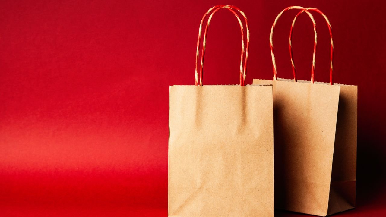 Simple brown paper bags with handle on a festive red backdrop, perfect for Christmas.