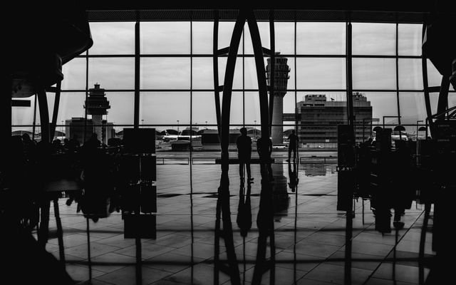 Black and white image of travelers silhouetted against large airport windows, capturing urban travel ambiance.