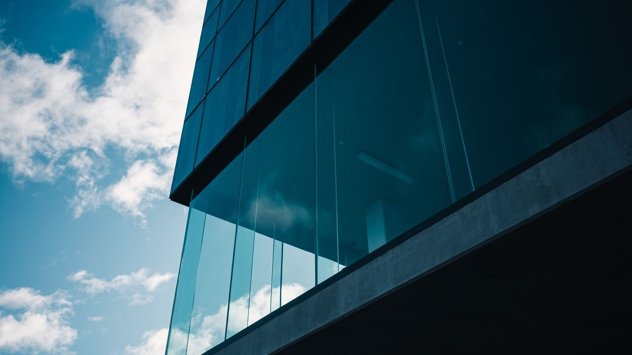 Low angle view of modern glass building against a vibrant blue sky with clouds.
