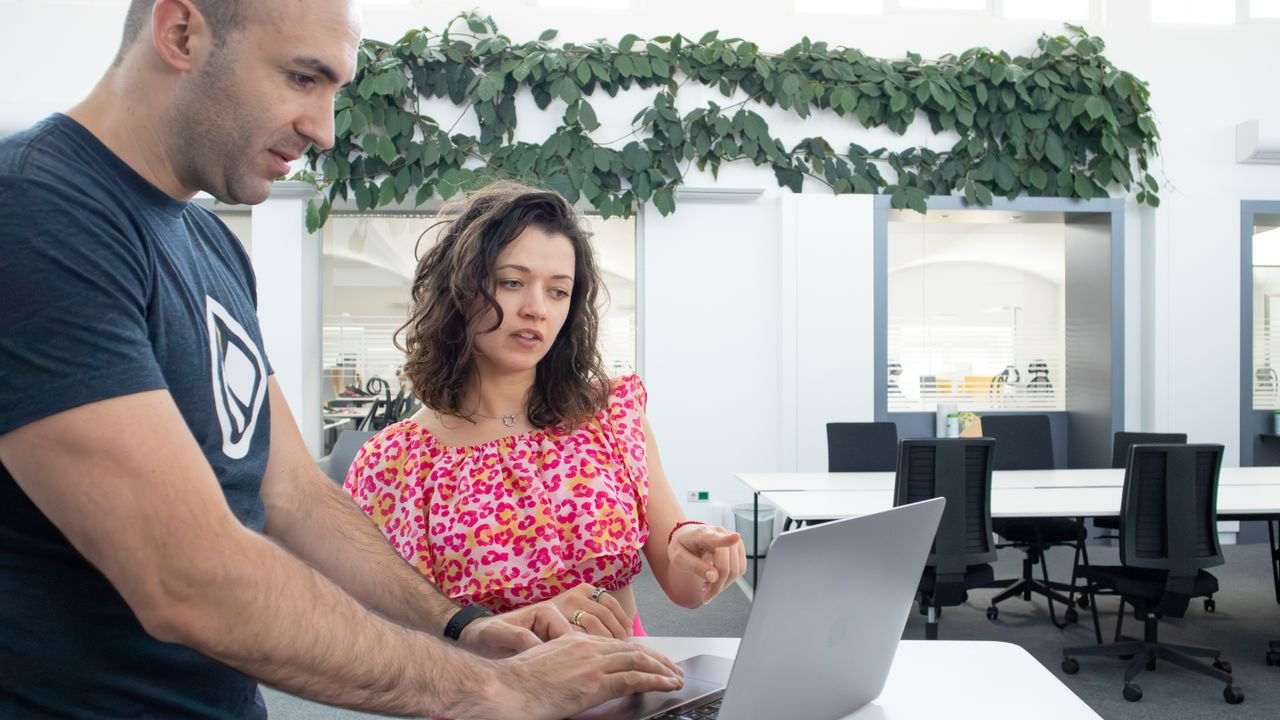 Two colleagues collaborate at a laptop in a bright, modern office space.
