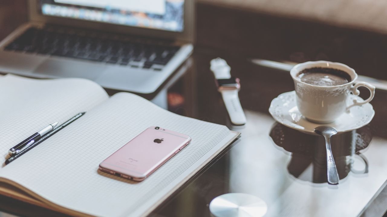 A comfortable desk setup with a laptop, smartphone, and coffee creating a cozy workspace atmosphere.