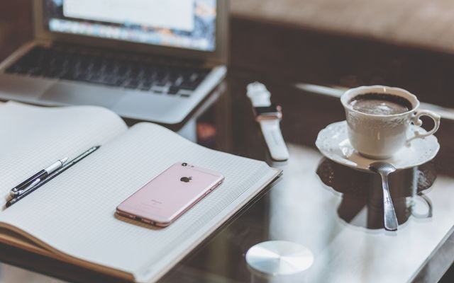 A comfortable desk setup with a laptop, smartphone, and coffee creating a cozy workspace atmosphere.
