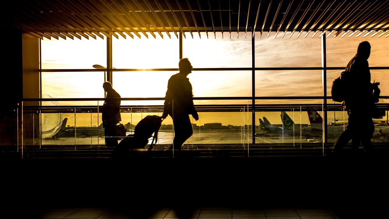 Travelers in silhouette pulling luggage at the airport during a beautiful sunset.