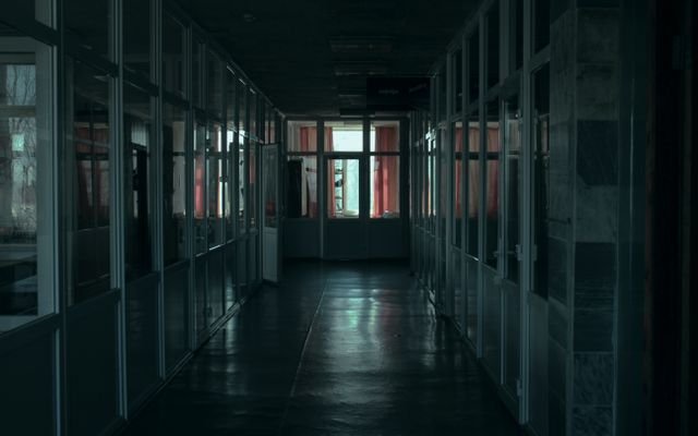 Gloomy indoor corridor with glass partitions and dim lighting in a modern office building.
