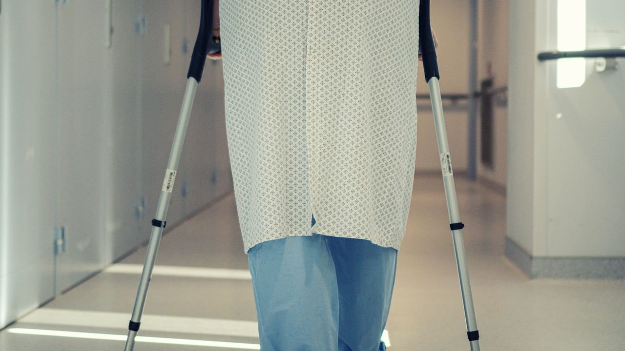 A senior patient using crutches to walk down a hospital corridor, symbolizing recovery and mobility assistance.