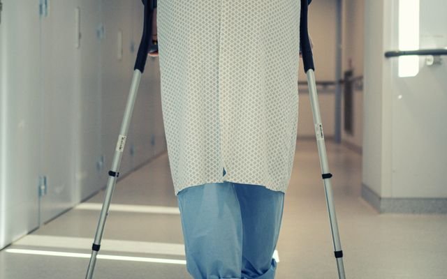 A senior patient using crutches to walk down a hospital corridor, symbolizing recovery and mobility assistance.