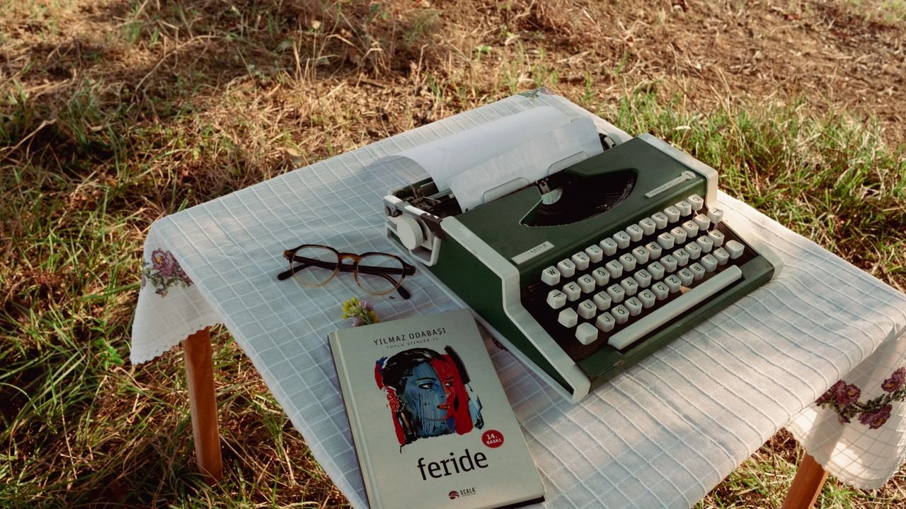 A green typewriter and book on a tablecloth-covered outdoor table.