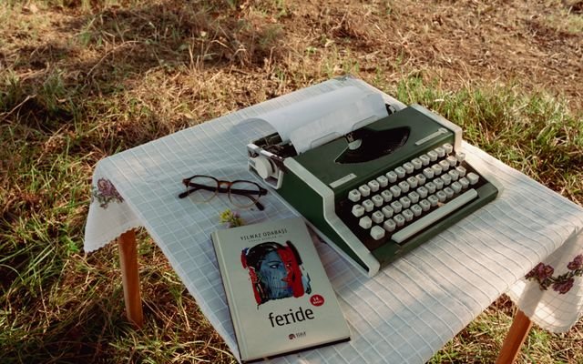 A green typewriter and book on a tablecloth-covered outdoor table.