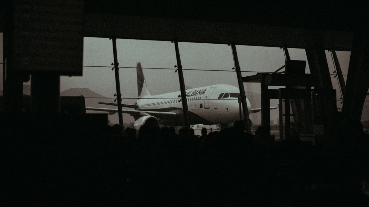 Silhouette of an airplane and waiting passengers inside an airport terminal at dusk.