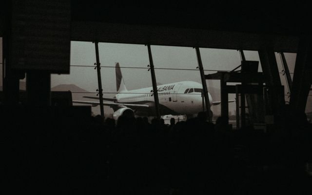 Silhouette of an airplane and waiting passengers inside an airport terminal at dusk.