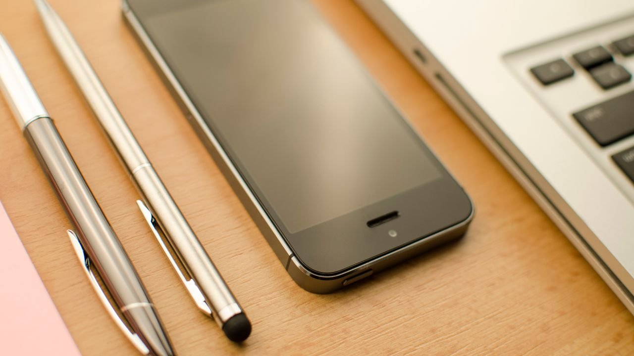 A neatly arranged desk featuring a smartphone, laptop, and pens in an office setting.