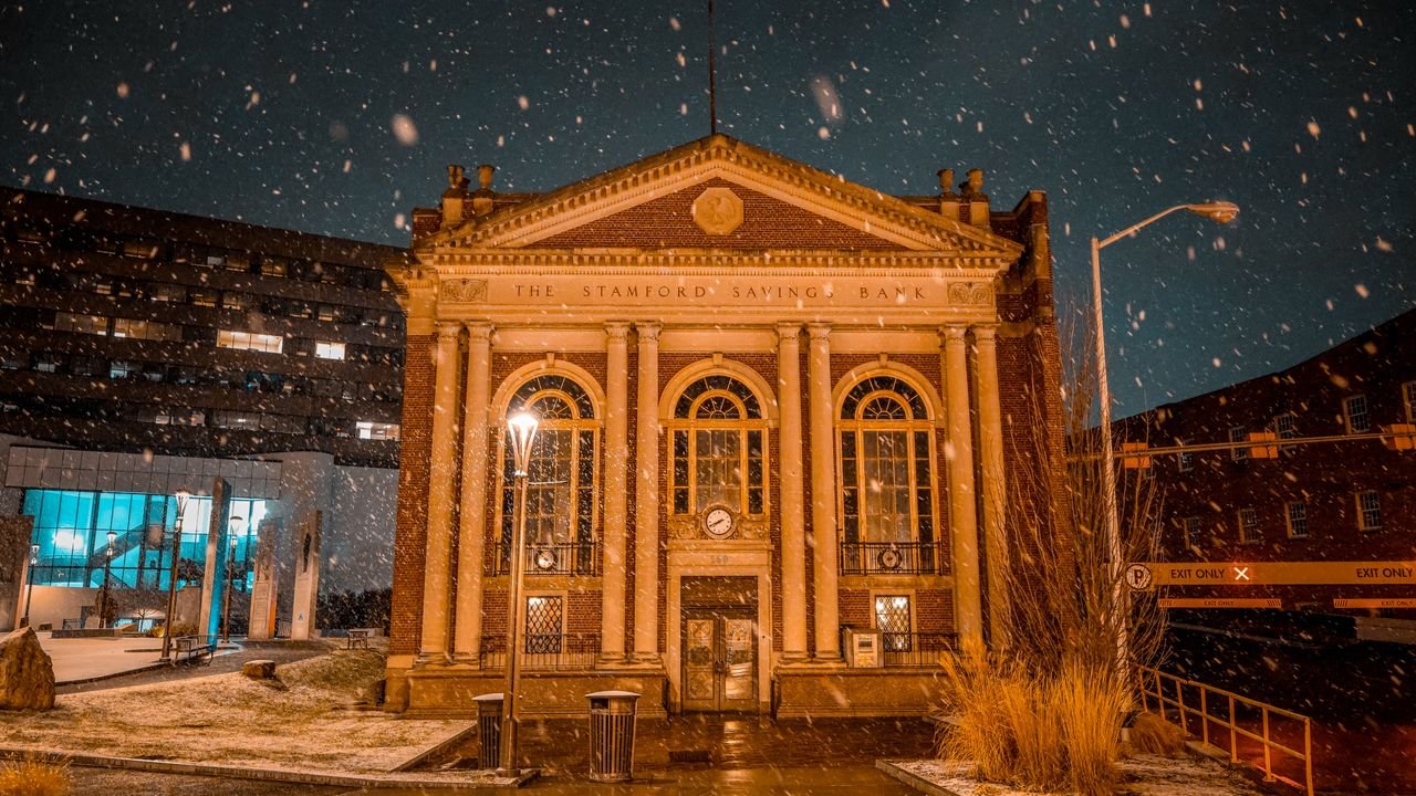 Historic Stamford Savings Bank illuminated at night during a snowfall in Stamford, Connecticut.