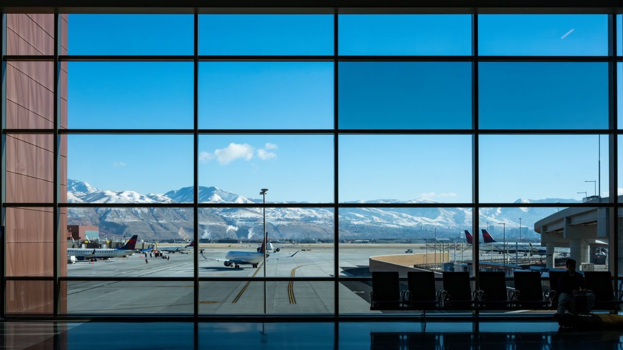 Panoramic view of airport terminal and runway with snow-capped mountains in the background.