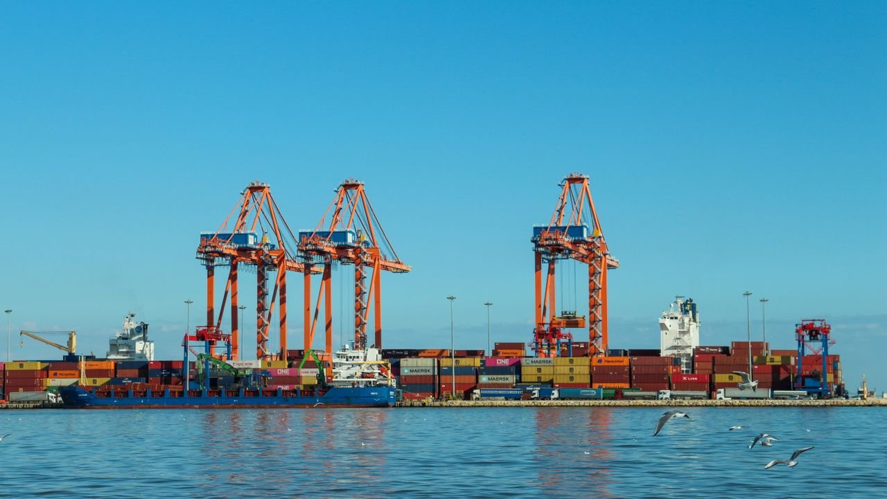 Colorful container port with large cranes and ships against a clear blue sky.