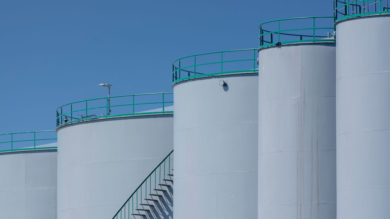 Large industrial storage tanks with green railings against a clear blue sky.