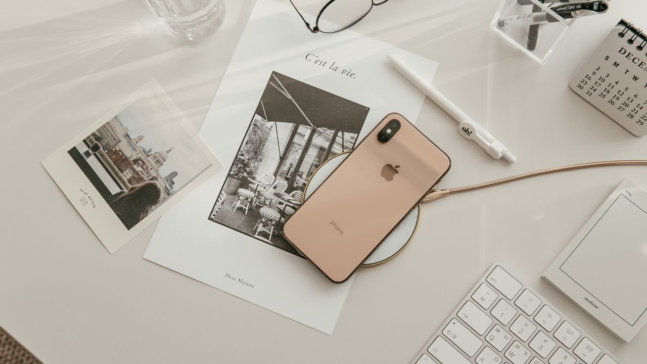 Aesthetic workspace featuring a smartphone, keyboard, and stationery in a warm, minimalist setup.