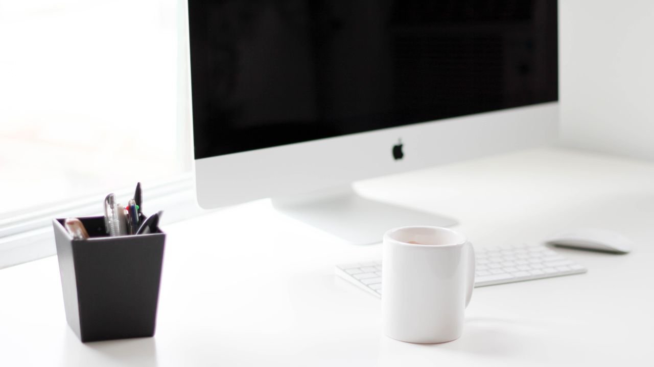 A minimalist work desk featuring a desktop computer, coffee mug, and office supplies.