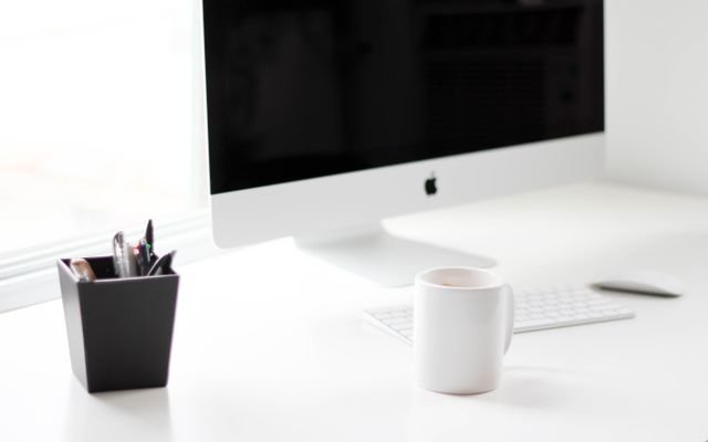 A minimalist work desk featuring a desktop computer, coffee mug, and office supplies.
